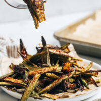 Fork holding up a few pieces of crispy oven roasted okra over a plate with more okra