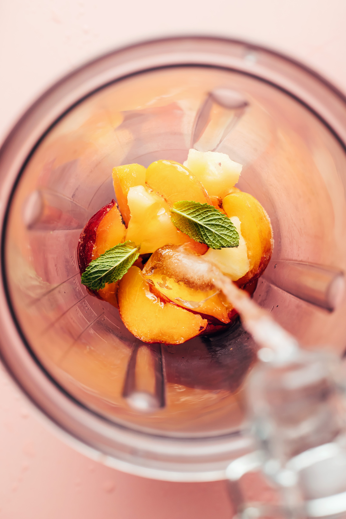 Pouring water into a blender with frozen fruit, mint leaves, and ice cubes