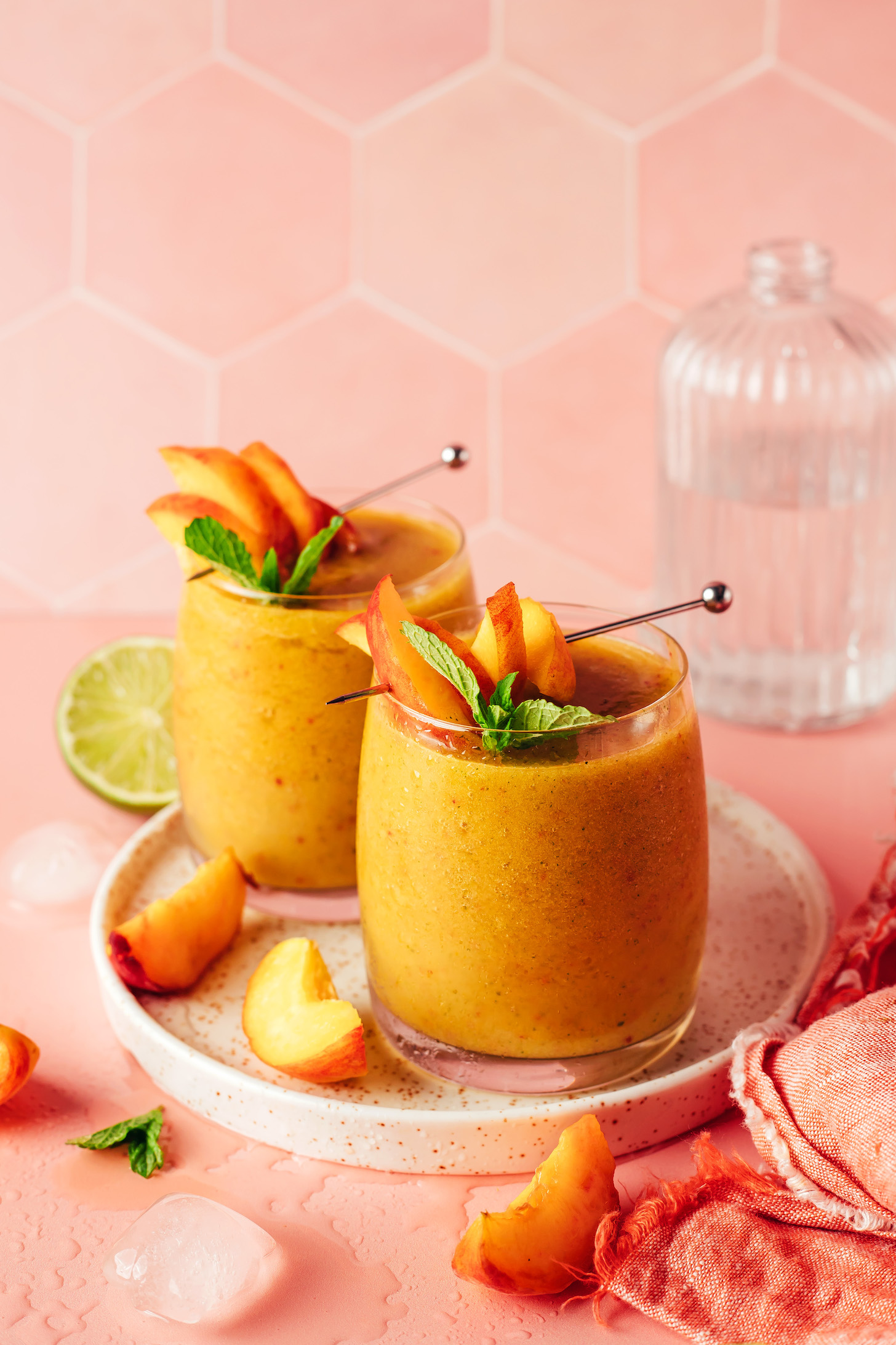 Two glasses filled with our frozen peach daiquiri recipe and topped with peach slices and fresh mint