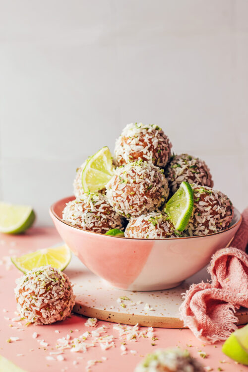 Bowl of coconut lime energy bites with lime wedges and shredded coconut scattered around