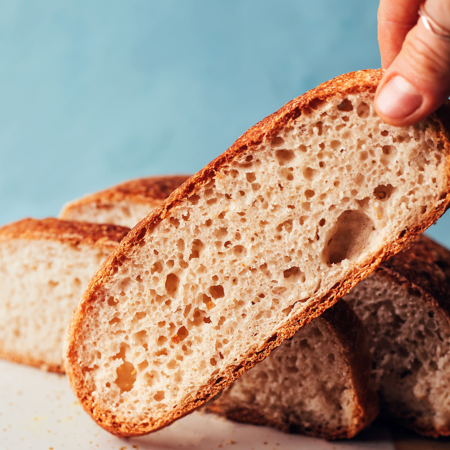 Holding up a slice of gluten-free artisan-style bread with more slices behind it