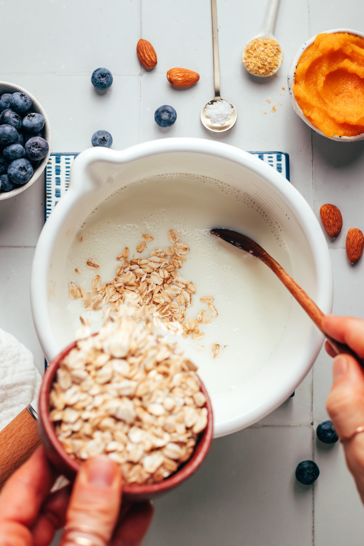 Pouring rolled oats into a saucepan of warmed almond milk