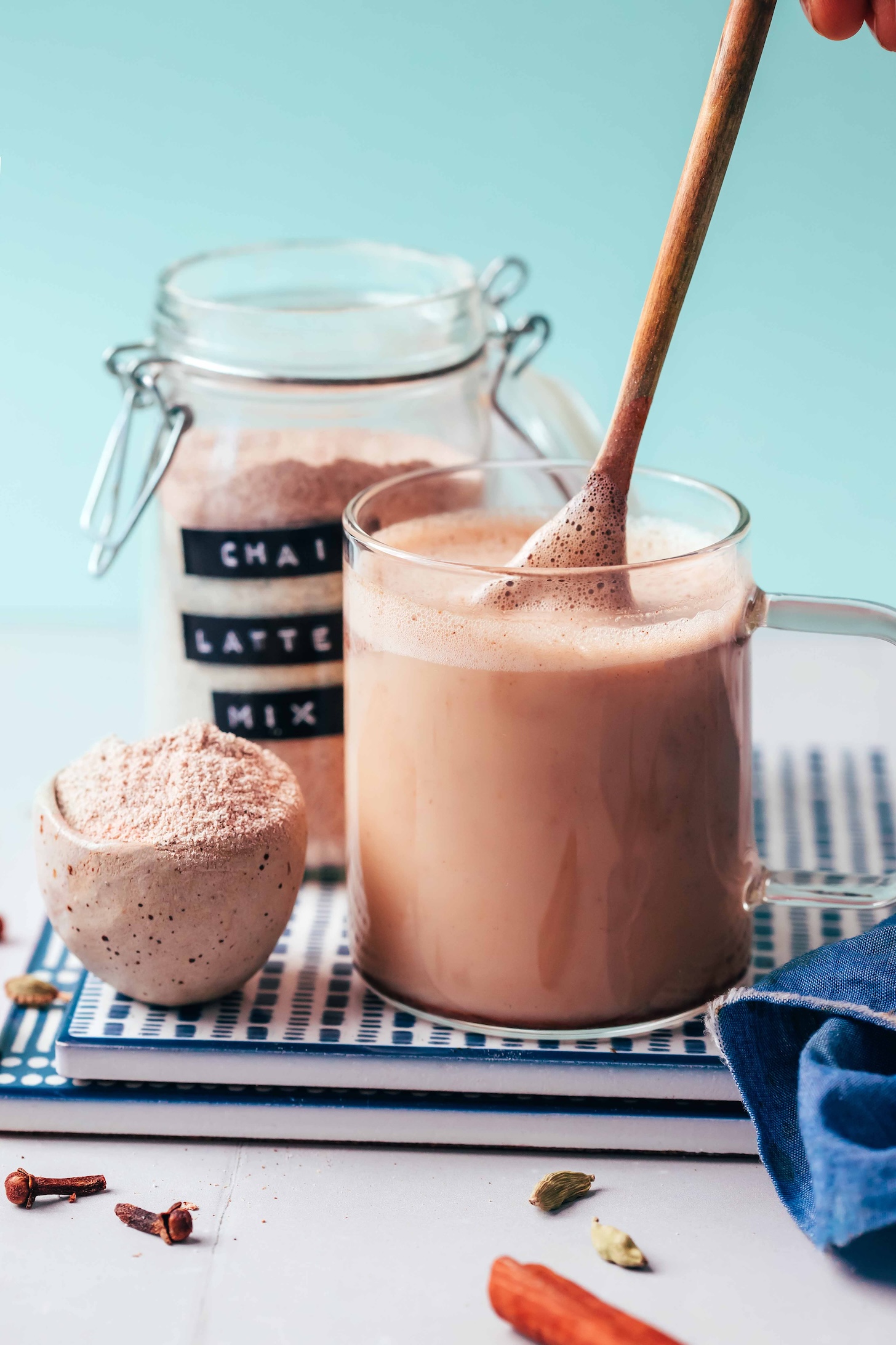 Using a small wooden spoon to make a mug of chai next to a small bowl and jar of Instant Chai Latte Mix