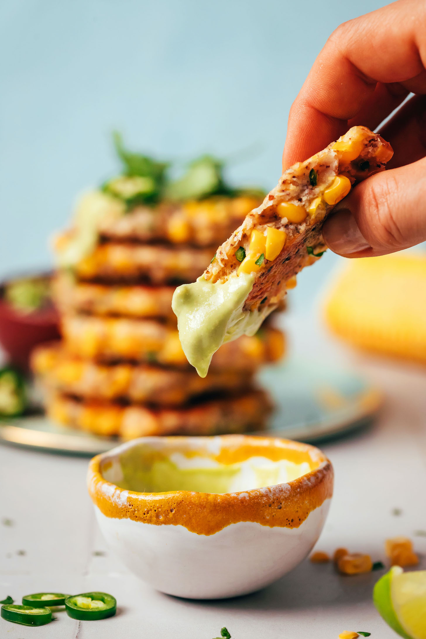 Hand holding up a partially eaten corn fritter freshly dipped in a bowl of cashew jalapeño sauce