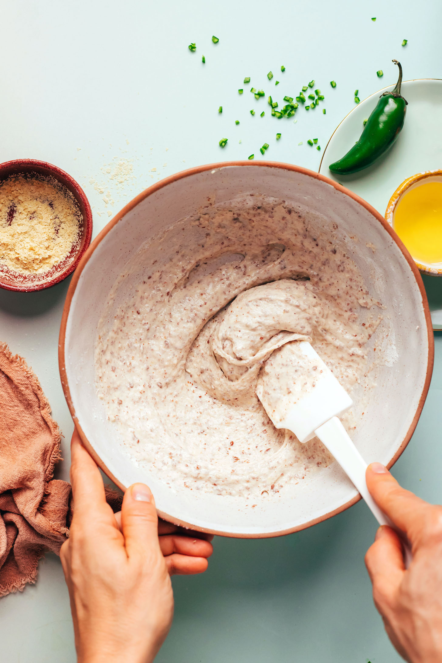Using a rubber spatula to stir vegan fritter batter in a bowl