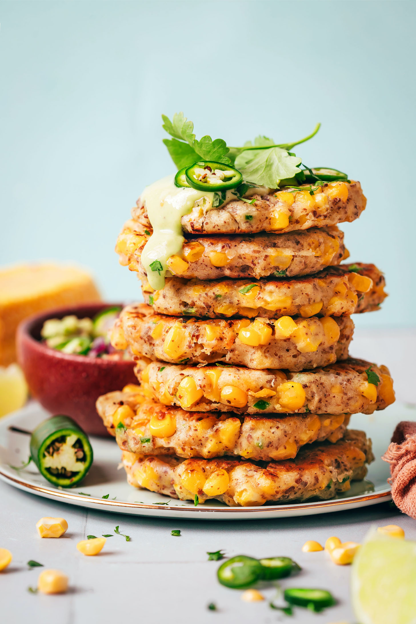 Stack of vegan jalapeño corn fritters topped with creamy cashew jalapeño sauce, sliced jalapeños, and cilantro