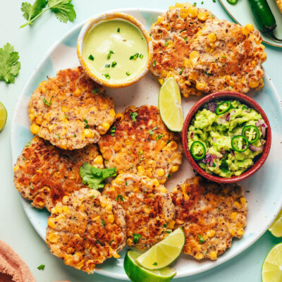 Plate of vegan ciorn fritters with lime wedges and small bowls of guacamole and cashew jalapeño sauce
