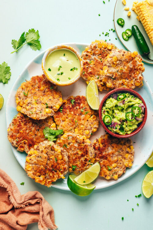 Plate of vegan ciorn fritters with lime wedges and small bowls of guacamole and cashew jalapeño sauce